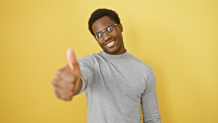 Smiling young man with glasses giving thumbs up against a bright yellow background.