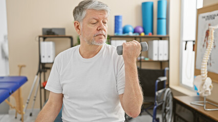 Obraz premium Mature man exercising with dumbbell in a rehab clinic interior to depict therapy and wellness.