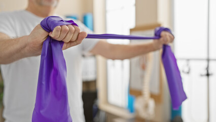 Mature man exercising with resistance band in a bright physiotherapy clinic