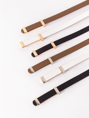 Thin leather women's belts in different colors with gold and silver buckles. Belts on white background