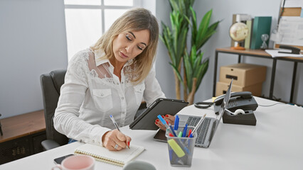 A professional woman works diligently in a modern office, surrounded by technology and office supplies.