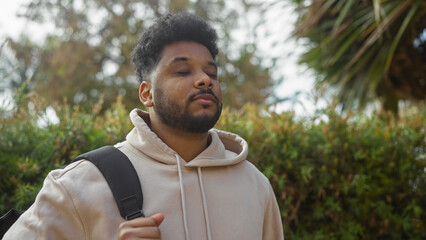 Handsome black man with backpack relaxing in a lush city park on a sunny day.