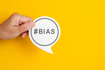 Hand holding real white speech bubble paper cut with BIAS word on yellow background