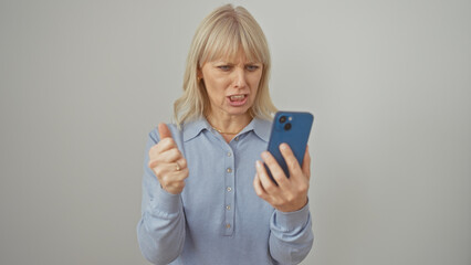 Fototapeta premium A frustrated woman in a blue shirt frowns at her smartphone against a white background.
