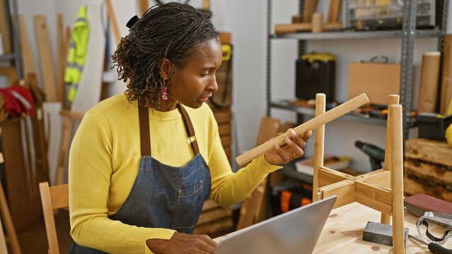 African american woman examines wood in a carpentry workshop surrounded by tools and workbench.