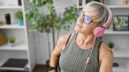 Mature woman with grey hair enjoying music with pink headphones in a modern office.