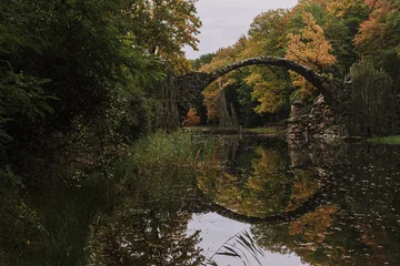 Reflection of a famous Rakotzbrücke bridge in water on a calm Autumn morning
