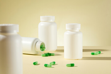 Medicine advertising, some white mockup medicine jars placed on light yellow table with scattered lay green vitamin capsules, in front is a blurred jars. Front view, copy space for text