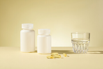 The photography at light yellow background features white unbranded supplement jars, a glass of water and yellow vitamin capsules. Front angle shot, blank space for adding text
