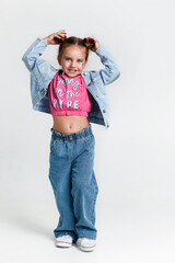 Full length little kid girl with hairstyle buns and glitter in pink t-shirt and jeans posing on white background