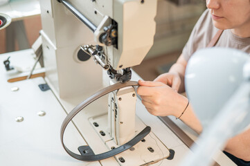 A woman tanner sews a leather belt on a sewing machine. Close-up of hands.