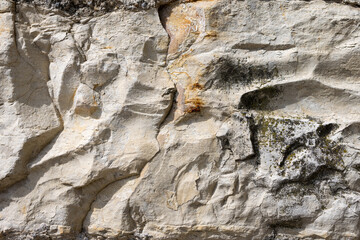 Detailed shot of a weathered rock face with visible signs of erosion and moss growth. The rough surface and varying shades of the rock provide insight into the natural weathering processes over time