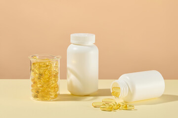 Mockup for fish oil advertisement with two white blank label bottles and glass beaker contains yellow supplement capsules, omega-3 in fish oil help protect eye health and reduce long-term inflammation