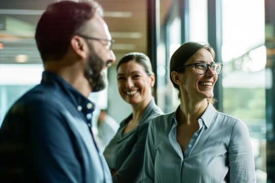Three colleagues smiling and conversing, captured in a candid moment in a bright, modern office space.