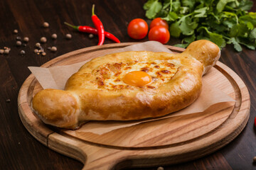 khachapuri with sulguni cheese, herbs and egg on a wooden surface. Georgian pie. Georgian pizza