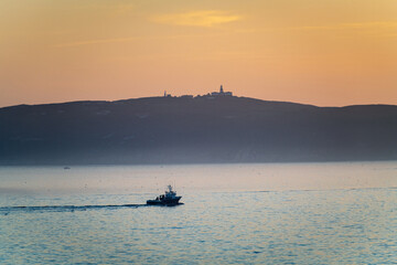 A lone fishing boat sails at sunset in the Ría de Pontevedra in Galicia at dusk, with the serene Ons Islands in the background. © Andrés García