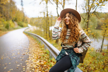 Happy Woman stay at road with thumb up in autumn sunny day. Hitchhiking. Traveler. Transportation