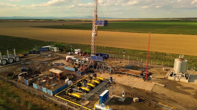 Aerial shot of shale gas drilling rig in a rural field in Romania. Fracking drill seen from above in the middle of a crop field. Drone footage of Hydraulic fracturing construction site.
