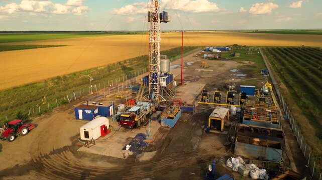 Aerial shot of shale gas drilling rig in a rural field in Romania. Fracking drill seen from above in the middle of a crop field. Drone footage of Hydraulic fracturing construction site.
