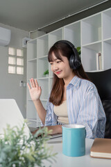 Young Student Engaged in Online Learning at Home with Laptop and Headphones, Waving Hand in Virtual...
