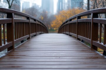 A tranquil wooden bridge leading over a calm waterway, surrounded by autumn foliage and urban skyline in the background.