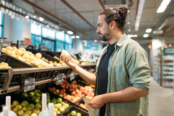 A young man is shopping at the supermarket. The guy picks vegetables and fruits from the counter in the store