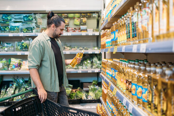 A young man is shopping at the supermarket. The guy chooses sunflower, olive oil from the counter...