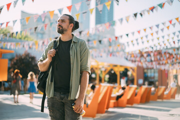 A young Caucasian man in an urban modern space. A handsome guy with a backpack walks around the city