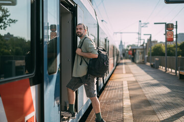 A man gets on a train on the platform. A young guy, a passenger with a backpack, enters the carriage from a high platform