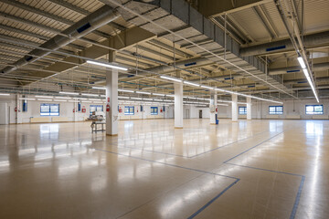Closed down empty factory interior manufacturing hall with tall ceiling, concrete beams. Wide angle shot, ceiling mounted neon lights, no people