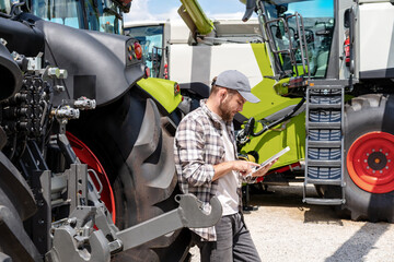 Agricultural equipment dealership. Agribusiness. Man leaned on a tractor wheel and using digital tablet. © Barillo_Images