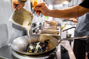 A person pouring creamy sauce into a pan with mussels on a stove, showcasing a cooking process in a kitchen setting. Perfect for culinary, cooking, and food preparation themes.