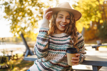 Attractive young smiling woman walking in autumn park with coffee. Travel, camping, nature concept