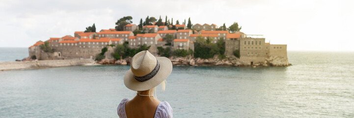 girl tourist in a hat looks from a top on the island of Sveti Stefan in Montenegro and the sea