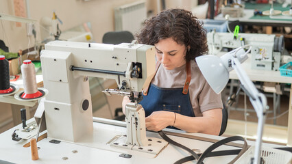 A woman tanner sews a leather belt on a sewing machine. 