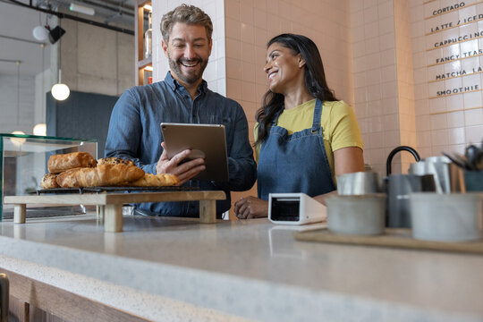Happy cafe business owners looking at finances on digital tablet