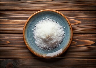 A simple yet elegant still life features a decorative plate with a mound of dry kosher salt, set against a clean wooden table top background.