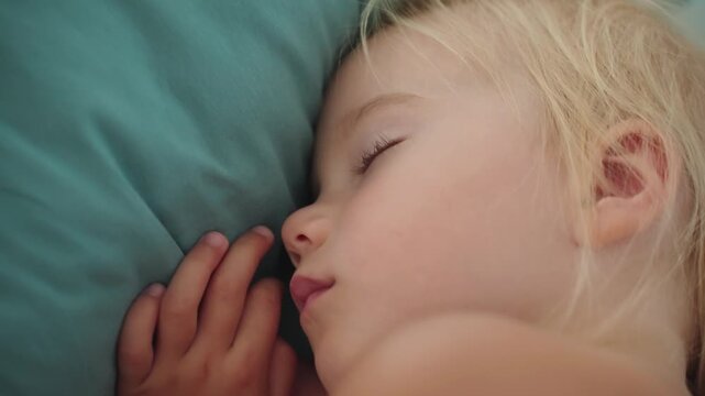 Close-up Beautiful sleeping face of blonde baby girl in crib. Baby napping, sound sleep of the baby, dry diaper all night. Parenting and child care. Daytime nap in bed with a pillow. Baby skincare.