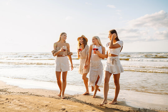 Group of female friends having fun at on the beach, celebrating bachelorette party, drinking wine at sunset. Holidays, nature, relax concept.