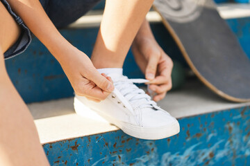 Closeup boy skater taking break and tying laces on his shoes while sitting at stairs