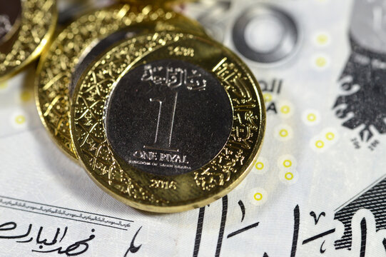 Pile of 1 one Saudi Arabia riyal coin currency features king Salman on  200 SAR two hundred Saudi Arabia riyals banknote bill features king AbdulAziz Al Saud and Vision 2030, economy and money concept