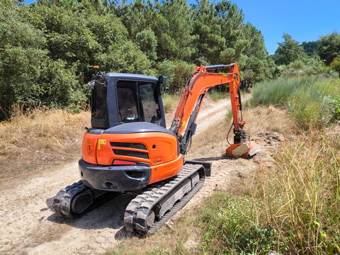 Mini escavadora de esteiras em a&ccedil;&atilde;o na limpeza eficiente das bermas de um caminho rural