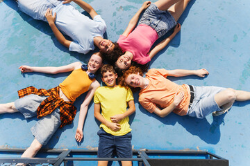 Top view of group of smiling kids relaxing, chilling, lying on sport ground