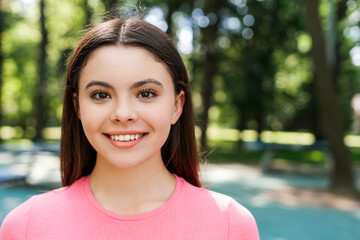 Smiling pretty teenager girl in pink t shirt looking at camera at the park