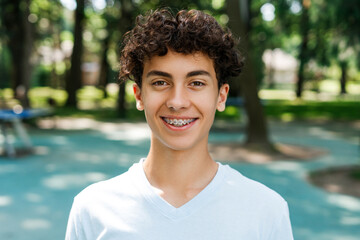 Happy teenager boy with braces positive smiling at camera outdoors