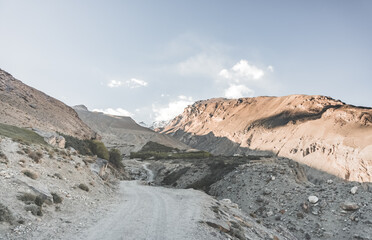 Dusty road in the mountains of Tajikistan in the evening among the mountains against the background of mountain ranges with snow and glaciers, mountain gorge with a road in Pamir