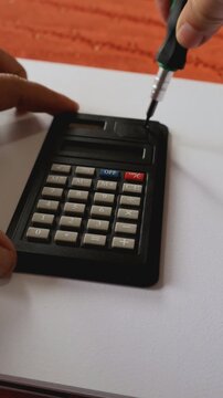 Caracas, Venezuela-07 de julio 2024: Primer plano de unas manos de mujer cambiando la bater&iacute;a o pila a una calculadora que dejo de funcionar. Video vertical.