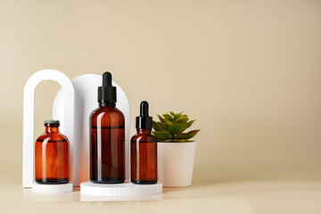 Set of brown glass bottles with essential oils on stand on beige background