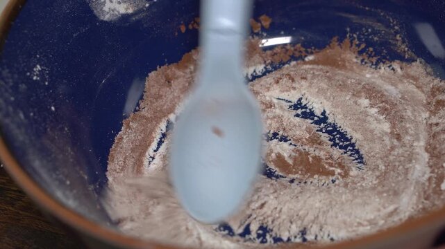 Mixing cocoa powder with white powders in a blue ceramic bowl. Cosmetic content of homemade dry shampoo for brown hair or bronzing powder for skin.