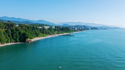 Scenic aerial view of the lush green coastline of Adjara, Georgia, with clear blue waters and vibrant beach life, surrounded by mountains.